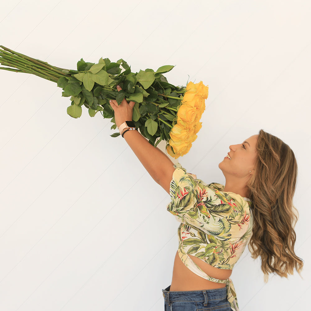 A woman is holding a yellow bouquet of long-stem roses