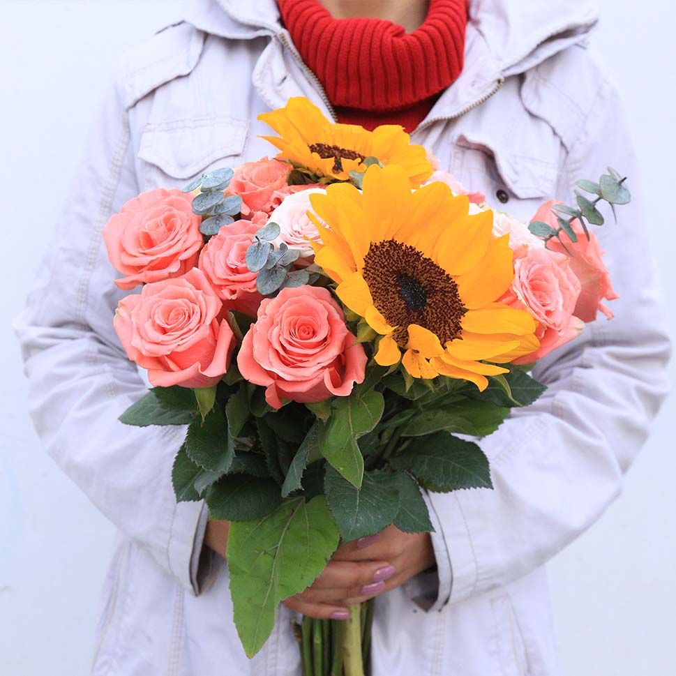 A woman is holding a Sonny Fresh bouquet of roses and sunflowers by Rosaholics