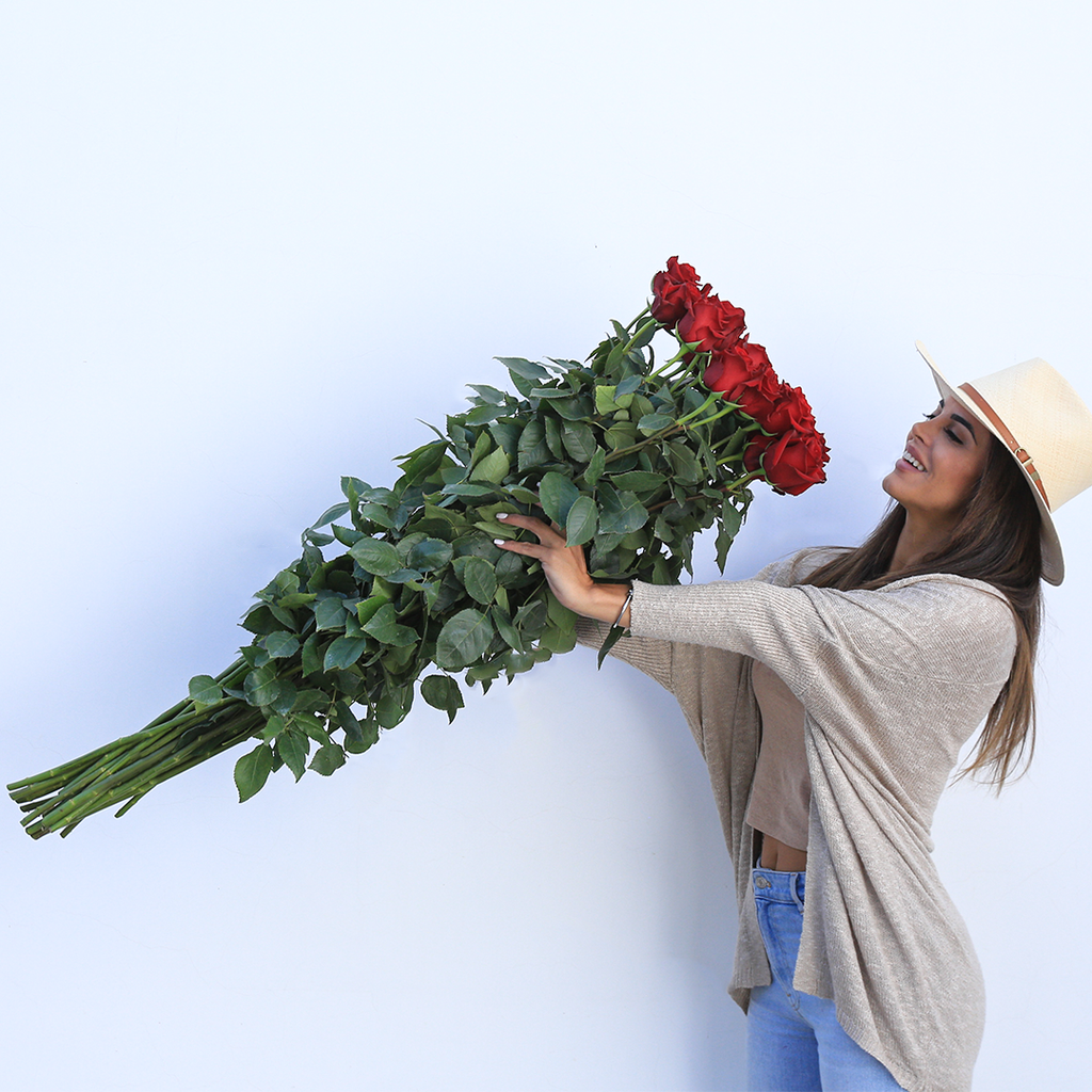 A girl is holding a bouquet of long stems red roses